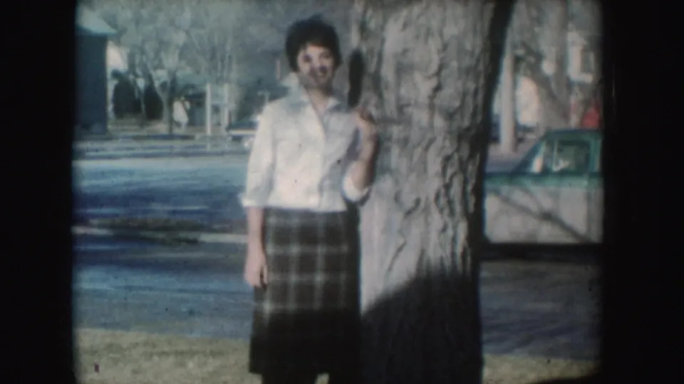 The woman remains posed beside the tree, with a parked car and bare trees visible in the South Dakota street background.