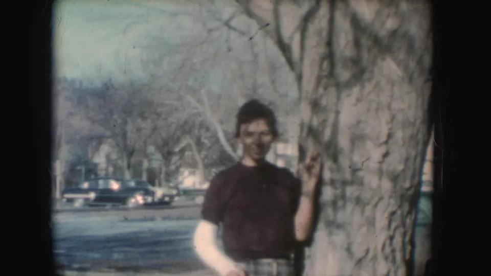 A second posed figure or changed outfit appears beside the tree on the same residential street in the supplied 1954 South Dakota clip.