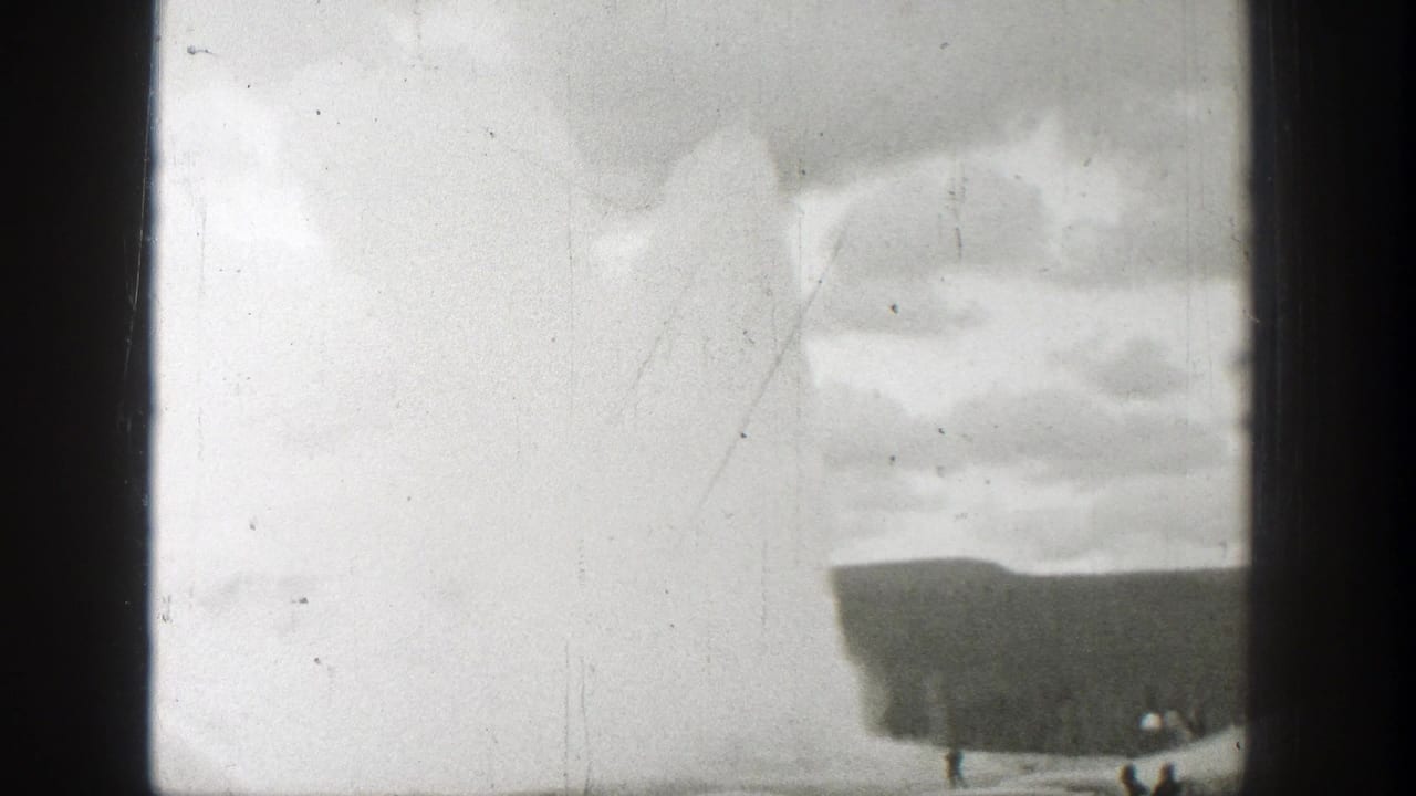 Geyser steam plume rising above a dark ridge with film borders and scratches.