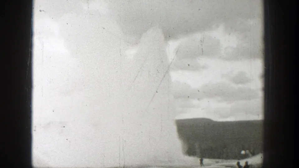 1939 Wyoming 8mm frame showing a geyser plume behind a low dark ridge, with tiny observers near the base.