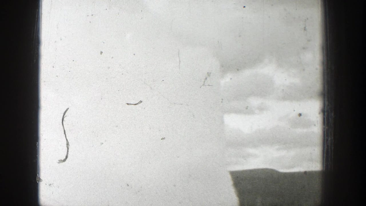 1939 Wyoming 8mm frame showing a pale geyser plume and cloudy sky partly blocked by dark window framing.