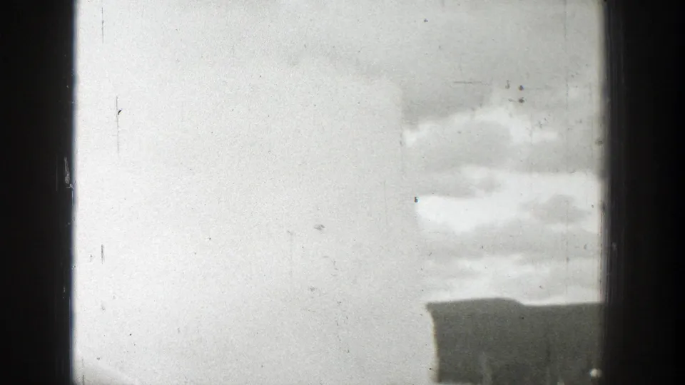 Black-and-white 8mm view of a geyser eruption in Wyoming, with steam and cloud forms behind a central window bar.