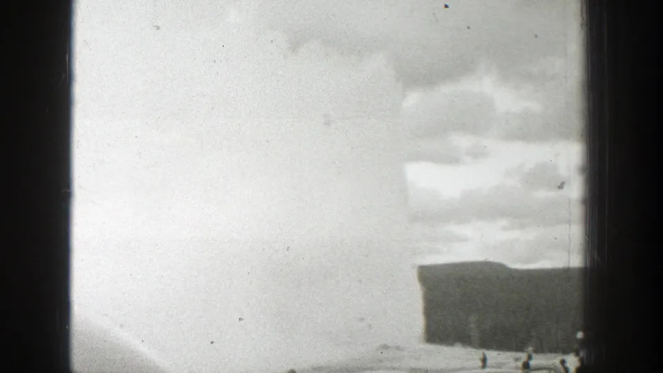 A soft, bright 1939 Wyoming geyser view with a low dark ground edge and vertical window framing in worn 8mm footage.