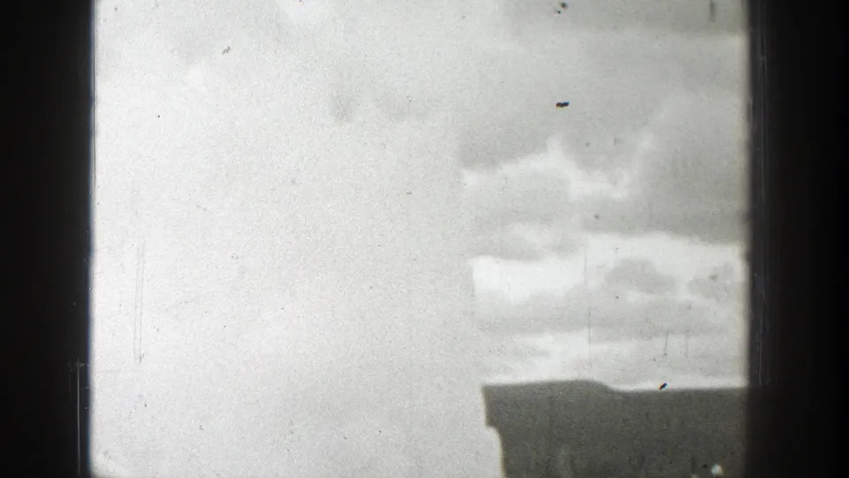Late-1930s Wyoming 8mm still showing geyser steam against clouds, bordered by dark window or vehicle framing.