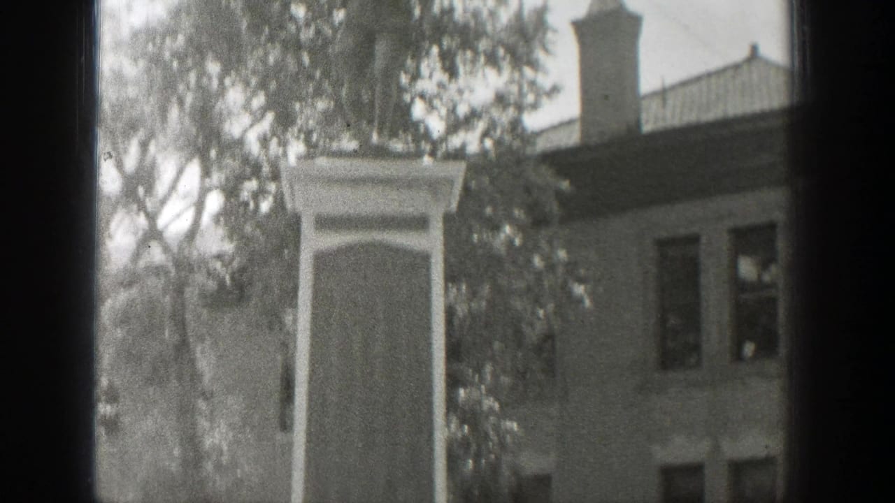 1939 Wyoming 8mm frame showing the upper portion of a stone memorial monument with trees and a multi-story building behind it.