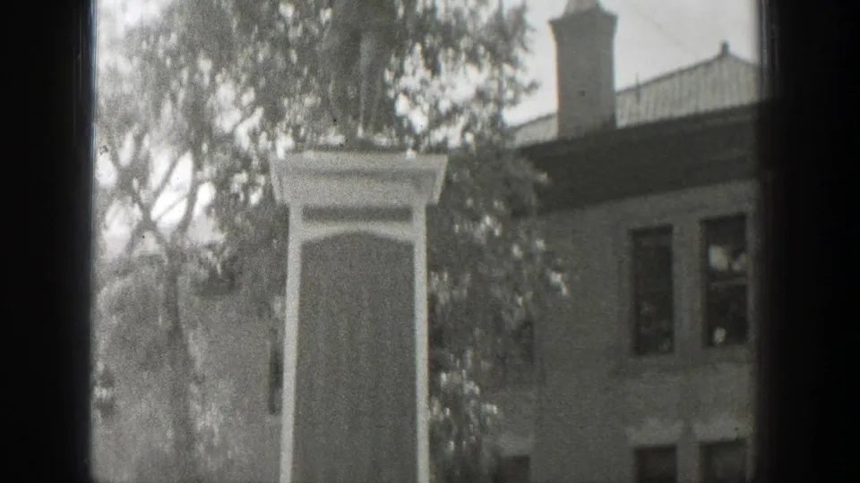 1939 Wyoming 8mm frame showing the upper portion of a stone memorial monument with trees and a multi-story building behind it.