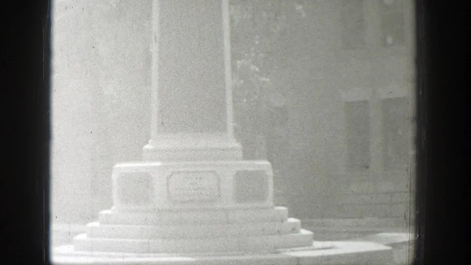 1939 Wyoming 8mm frame with a brighter exposure on the monument base, stepped pedestal, unreadable plaque, and building behind it.