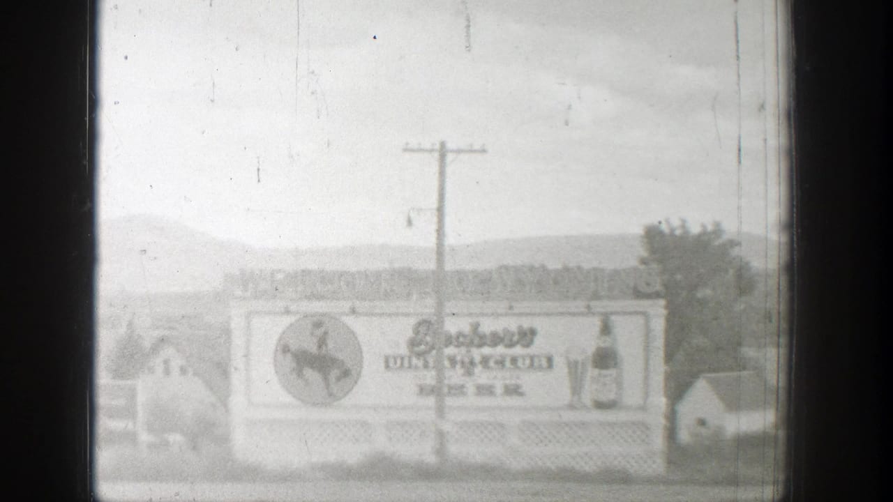 1939 Wyoming 8mm frame showing a Beckers Club Beer billboard with cowboy emblem, bottle art, utility pole, houses, and distant hills.