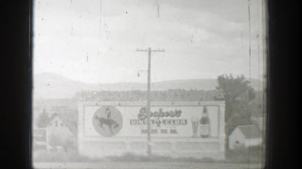 1939 Wyoming 8mm frame showing a Beckers Club Beer billboard with cowboy emblem, bottle art, utility pole, houses, and distant hills.