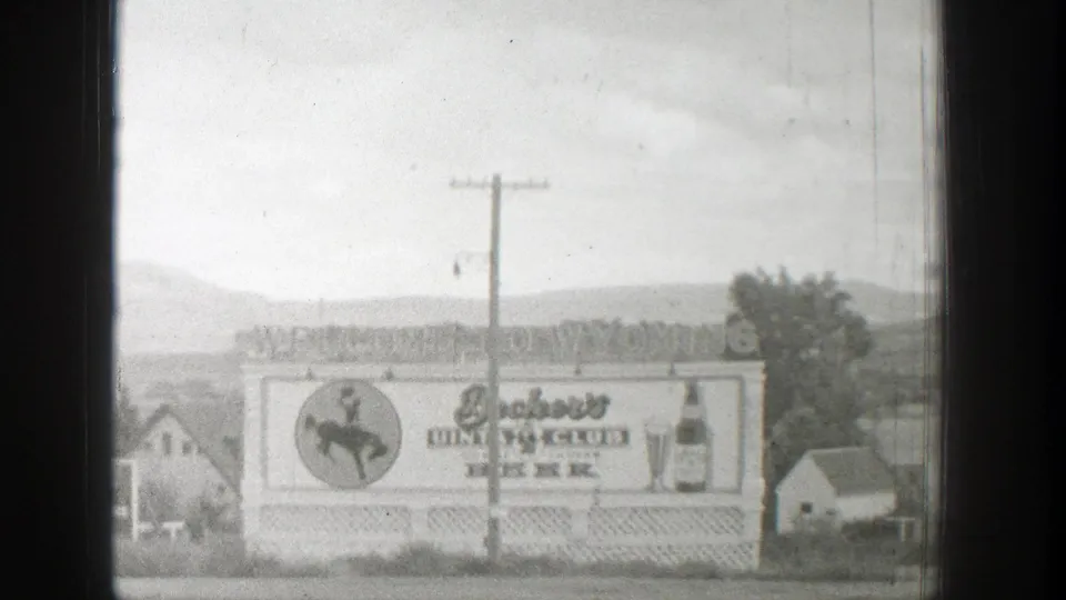 Final black-and-white frame of the 1939 Wyoming billboard scene, showing Club Beer branding, bottle art, rural houses, trees, and hills.