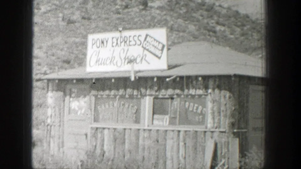 1939 Wyoming home-movie frame of a small wooden roadside stand with visible Pony Express Chuck Shock and Home Cooking signage.