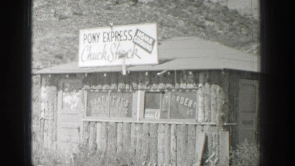 Black-and-white 8mm frame of the Wyoming roadside stand, with the sign and rough wood siding filling most of the view.