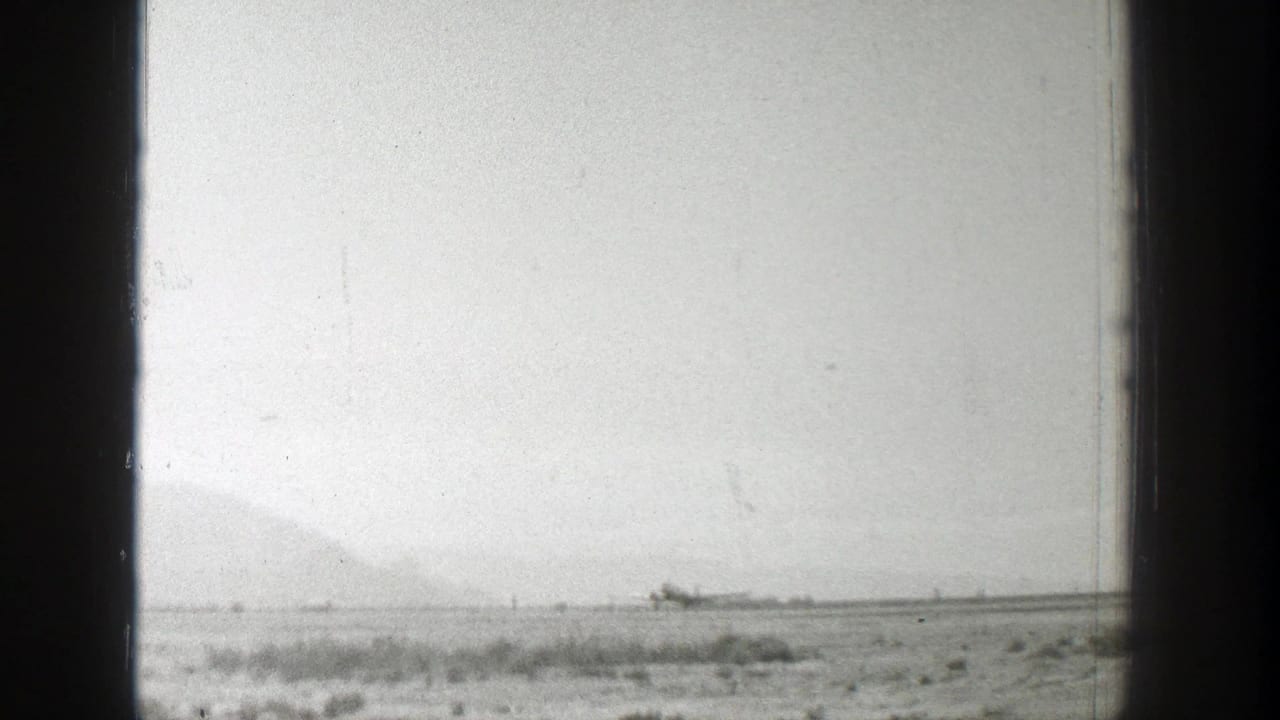 Distant propeller airplane on a grass field with hazy mountains behind it.