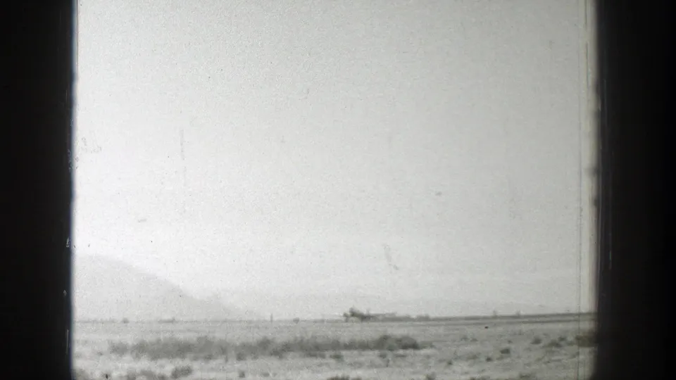 1939 Wyoming 8mm frame showing a small propeller airplane far across a grassy airfield, seen through dark vertical framing.
