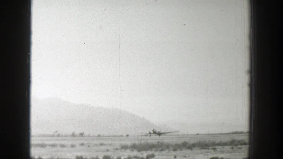 Distant 1939 Wyoming airfield view with a small propeller aircraft near the horizon and hazy mountains behind it.