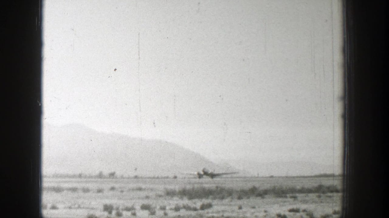 1939 Wyoming home-movie frame showing a distant propeller airplane on a rural airstrip below hazy mountains.