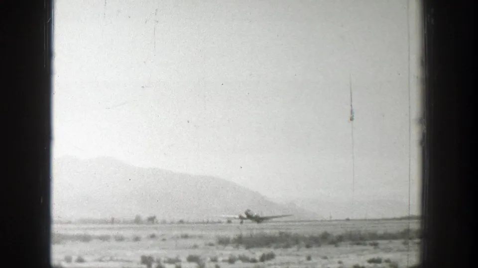 1939 Wyoming frame with a small propeller aircraft crossing a remote runway beneath a clear sky and distant mountains.