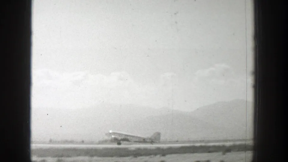 Wide 1939 Wyoming home-movie view of a propeller airplane near takeoff on a remote airstrip with mountains beyond.