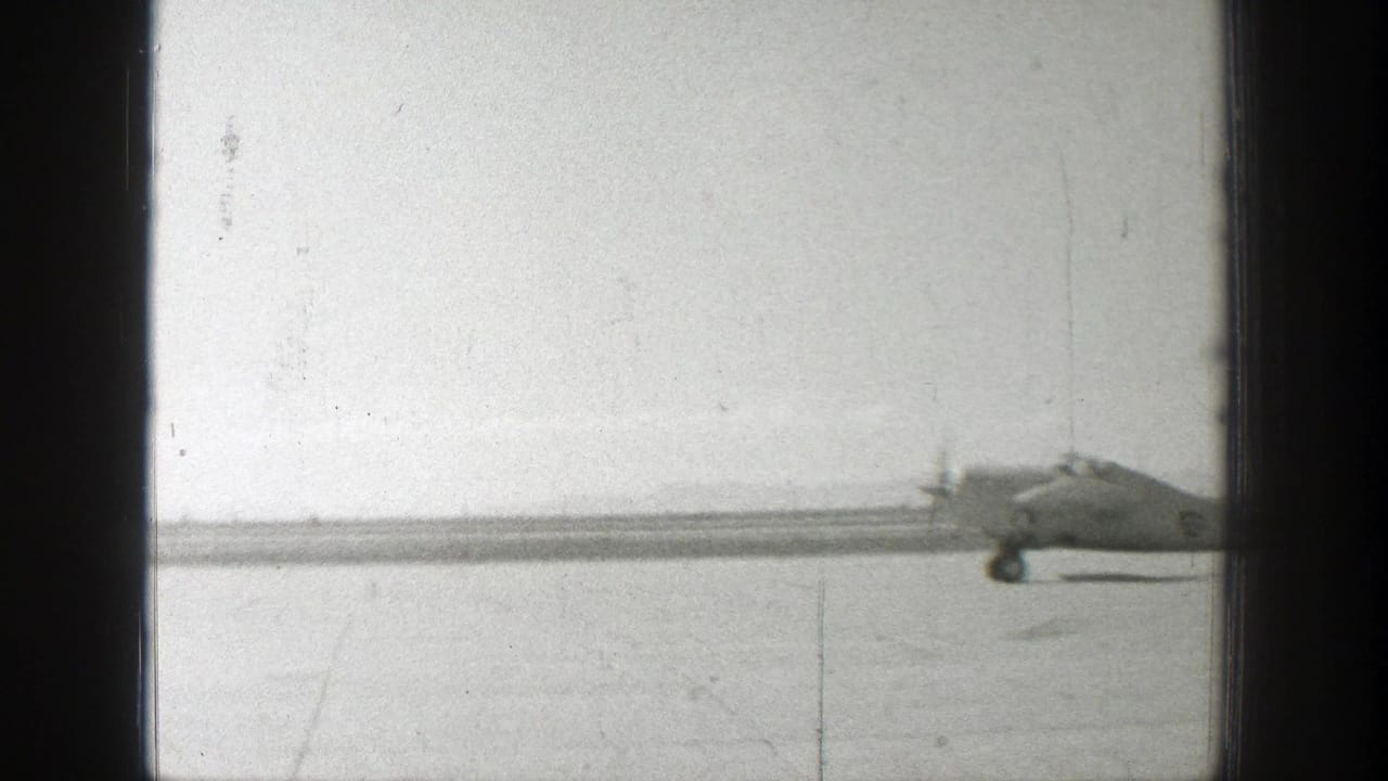 Propeller airplane on a flat airfield seen through dark 8mm frame borders.
