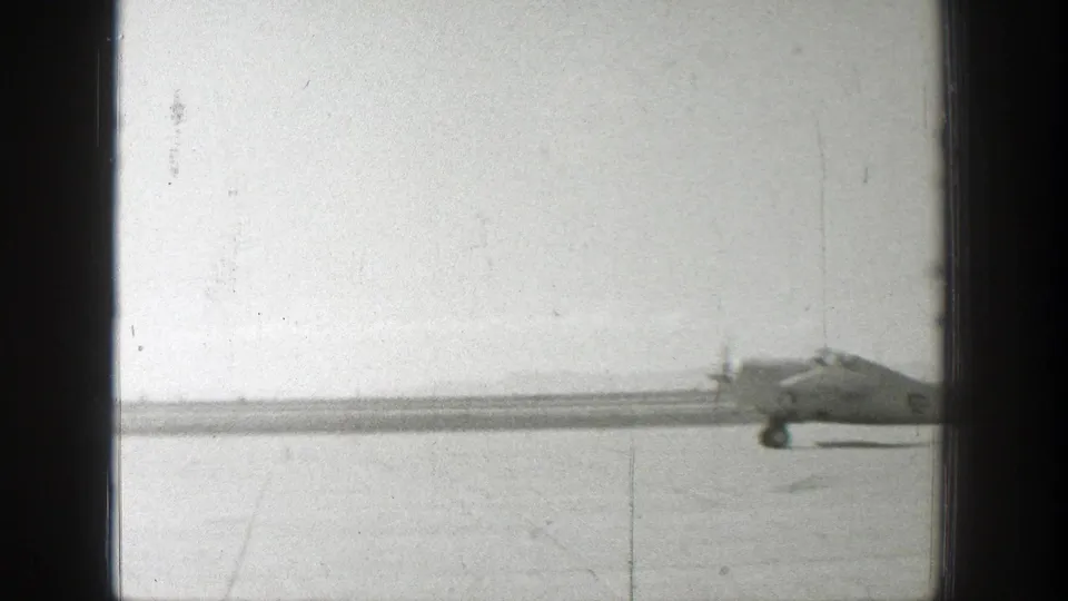 1939 Wyoming home-movie frame showing a distant Army airplane on a flat airfield under a pale sky.