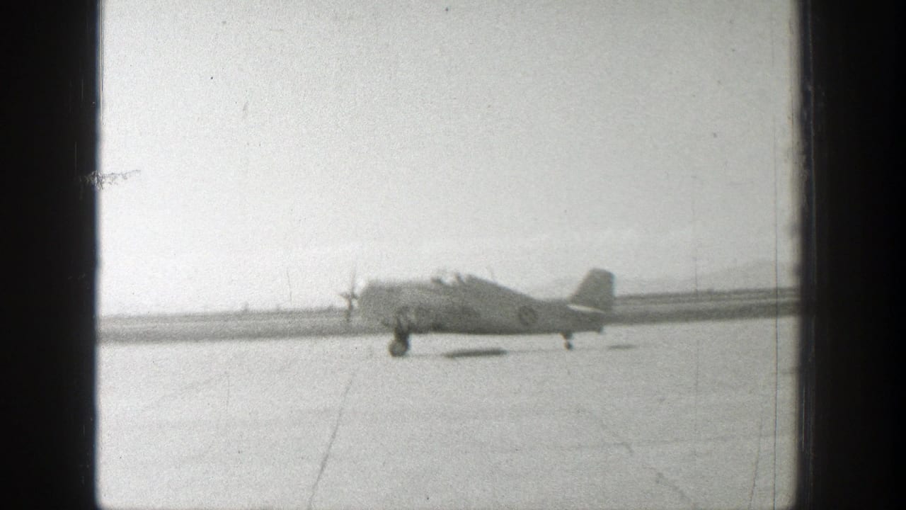 Distant propeller airplane moving along a flat runway or airstrip.