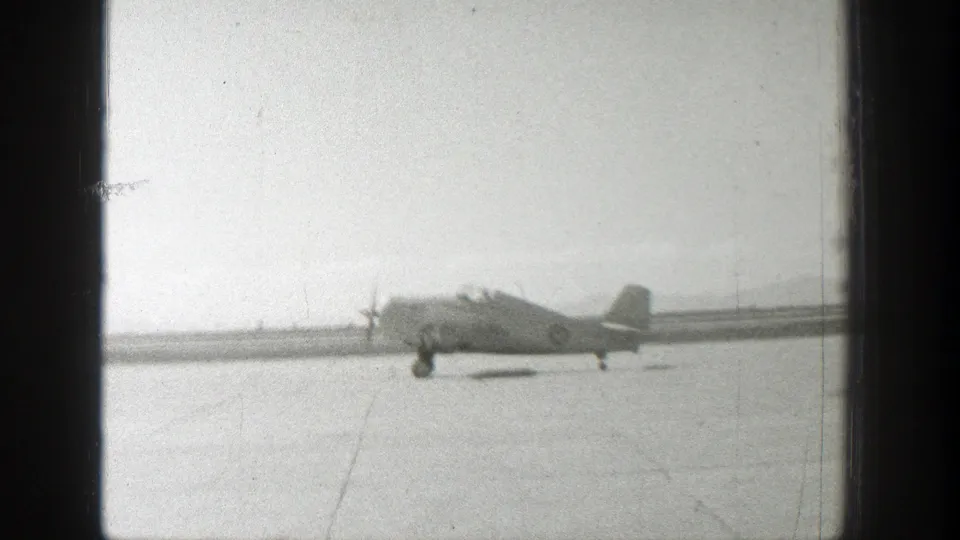 1939 Wyoming frame with a distant Army airplane taxiing or beginning takeoff across a sparse airfield.
