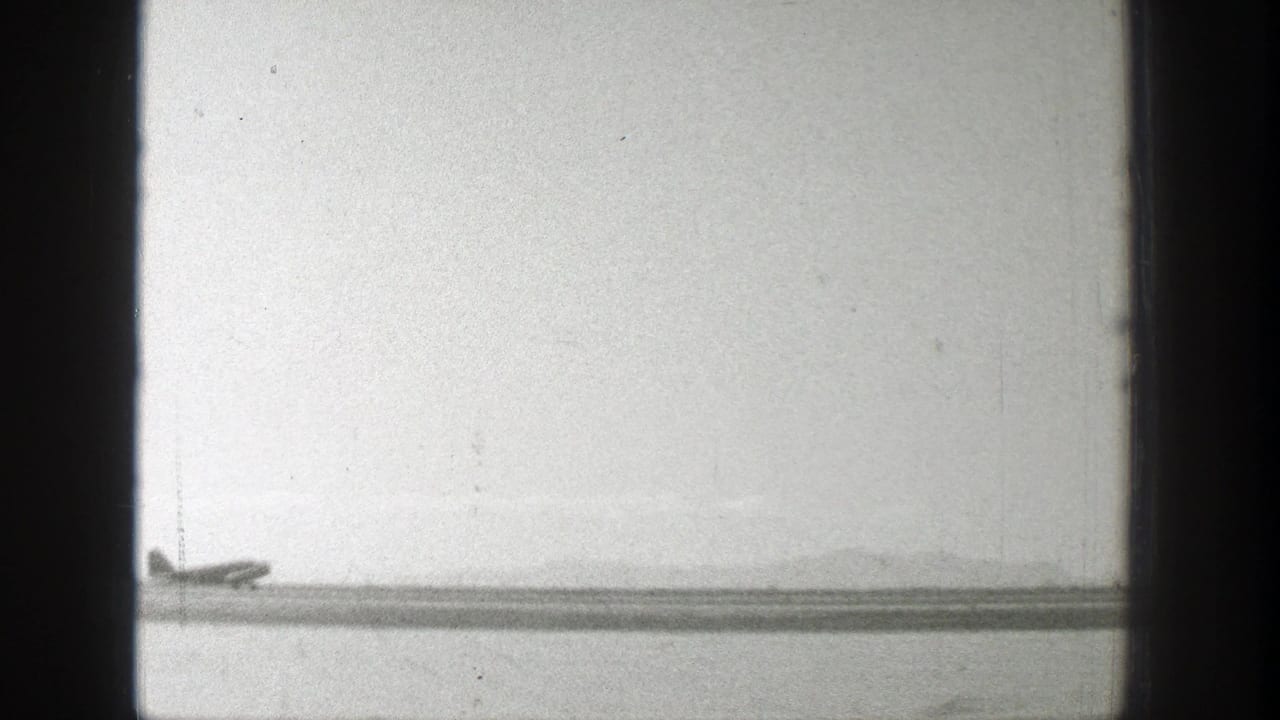 1939 Wyoming 8mm frame showing a distant propeller plane near a runway with horizon haze and heavy film-edge borders.