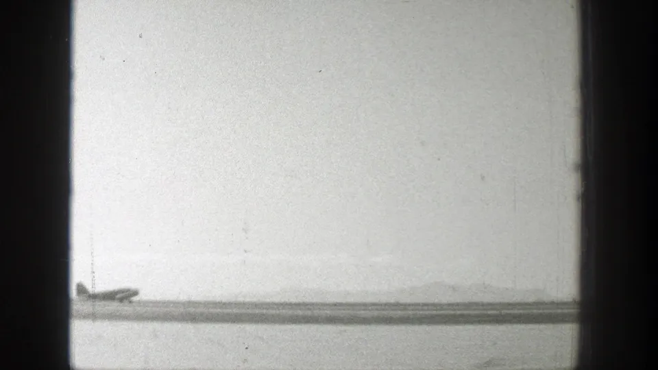 1939 Wyoming 8mm frame showing a distant propeller plane near a runway with horizon haze and heavy film-edge borders.