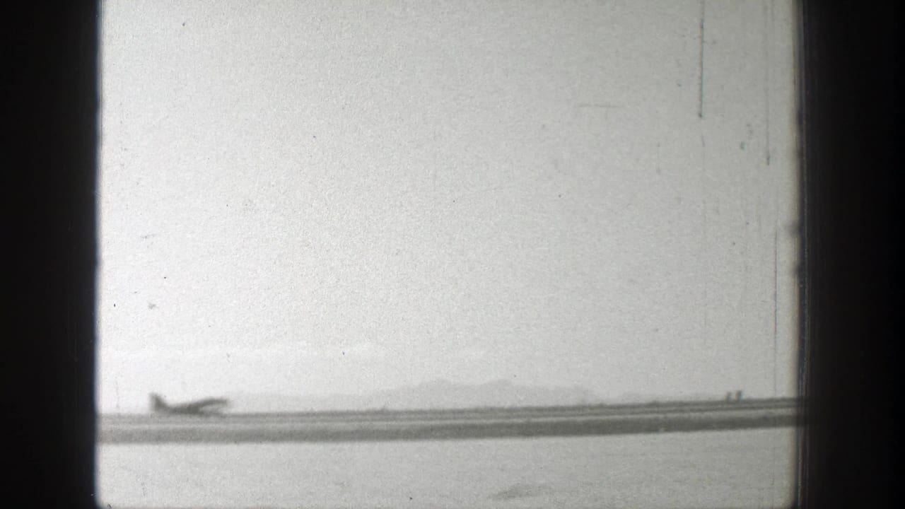 Small propeller plane crossing a distant runway under a pale sky.