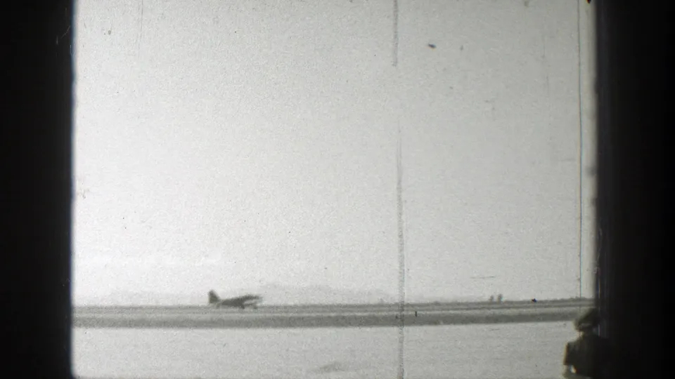 1939 Wyoming airfield view with a small propeller plane, runway, faint background figures, and visible 8mm wear.