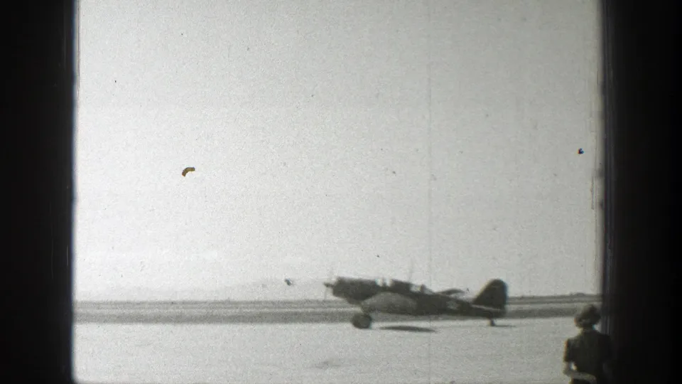 1939 Wyoming home-movie frame showing a small propeller plane on an airfield with runway and open sky behind it.