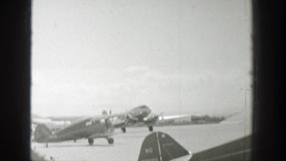 1939 Wyoming airfield view with a propeller aircraft on the tarmac and a marked aircraft tail partly visible in front.