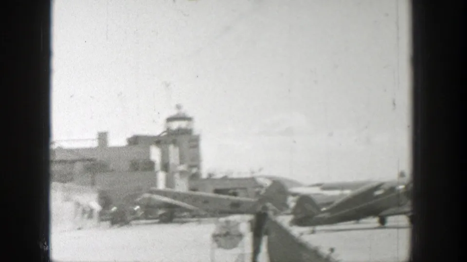 1939 Wyoming home-movie view of small aircraft parked or taxiing near a control tower at an airfield.