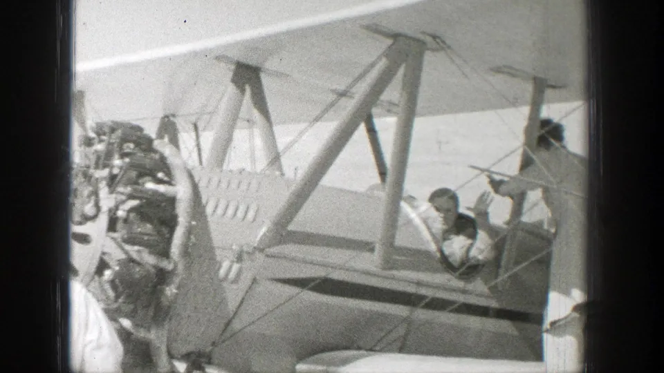 1939 Wyoming 8mm frame showing a biplane with exposed radial engine, wing struts, and a person seated in the open cockpit.