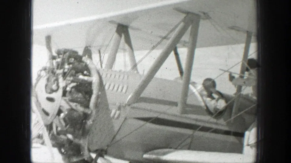 The biplane's exposed radial engine and open cockpit are visible, with a person seated inside and another figure partly at the right edge.