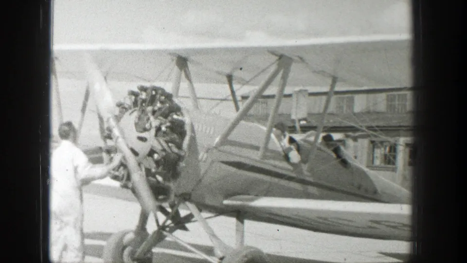 A man in a white shirt stands at the front of the 1939 Wyoming biplane near the propeller while people sit in the open cockpit.