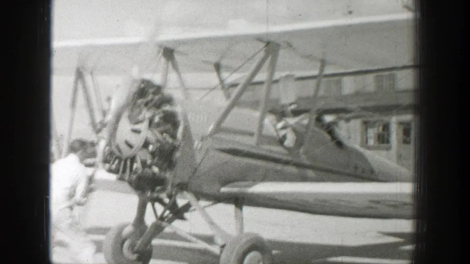 The biplane is seen from the side with its radial engine, landing gear, open cockpit, and people positioned near the nose and fuselage.