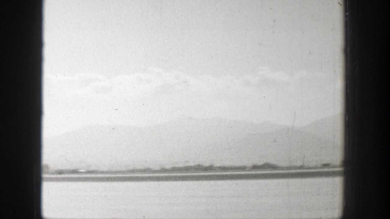 Distant airplane on a runway seen through dark vertical window framing.