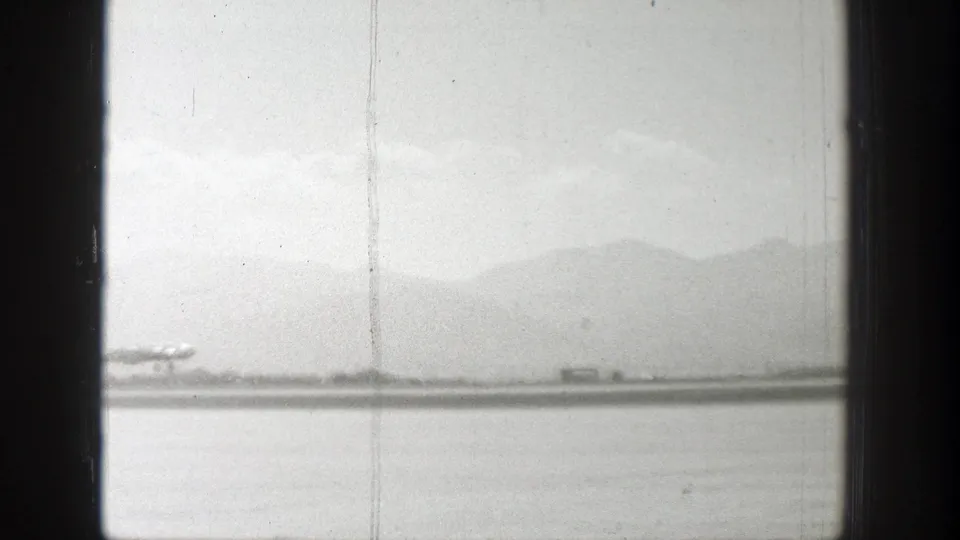 A silver propeller aircraft appears near the runway in 1939 Wyoming footage, with mountains and a pale cloudy sky behind it.