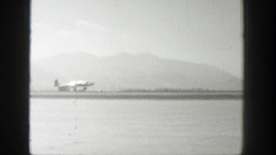 The home-movie frame shows the aircraft closer to the camera, moving along the runway with the western mountain landscape behind it.