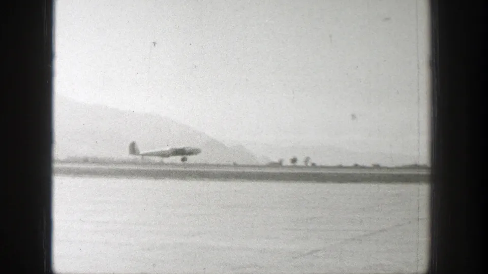 The aircraft appears just above or at the runway in 1939 Wyoming 8mm footage, with distant mountains and dark window framing visible.