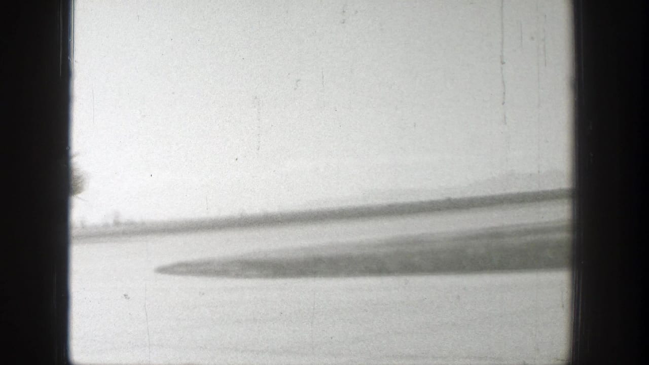 A soft, partially obscured view shows a runway area and possible aircraft wing or airfield surface within dark 8mm frame edges.