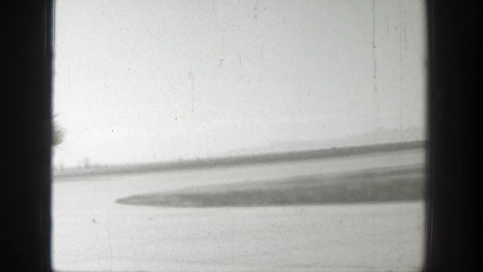 A soft, partially obscured view shows a runway area and possible aircraft wing or airfield surface within dark 8mm frame edges.