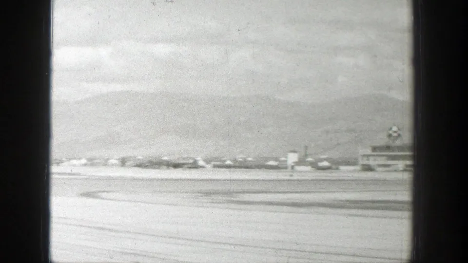 The Wyoming airfield is visible after the aircraft passes, with runway pavement, low buildings, and mountains in the background.