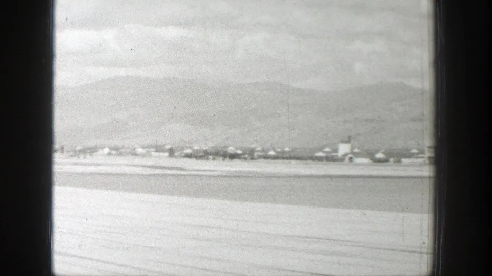 1939 Wyoming aerial view through aircraft window framing, showing a distant settlement, valley floor, and mountain backdrop.