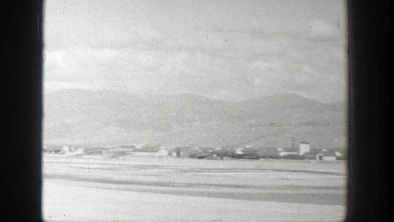 Distant buildings and mountain slopes seen through dark vertical window frames.