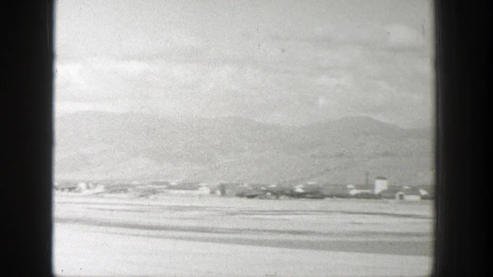 Aerial home-movie frame of a Wyoming town below mountain slopes, partially divided by aircraft window framing.