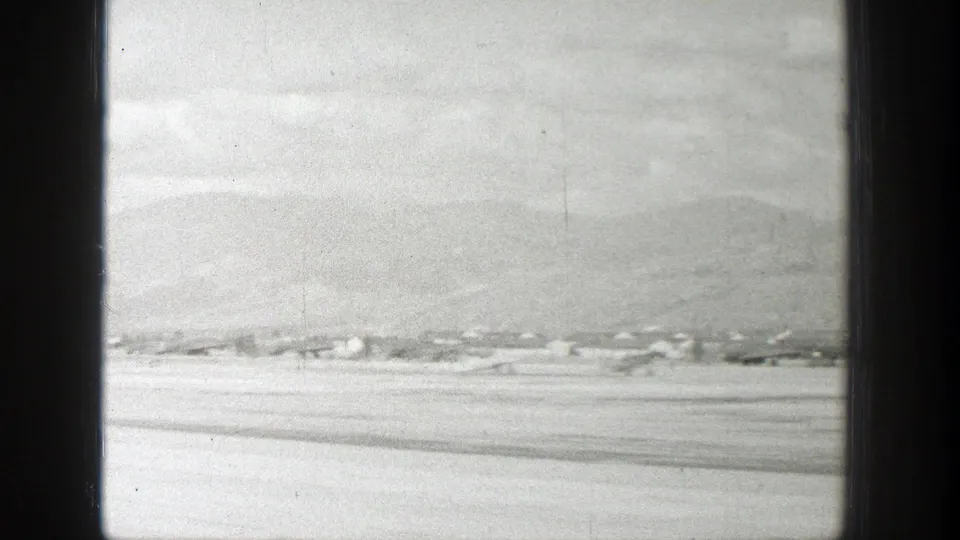 1939 Wyoming aircraft view showing a pale valley, low buildings, and hazy mountains in soft black-and-white 8mm footage.