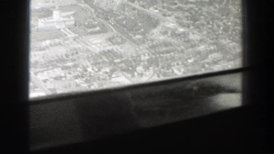1939 Wyoming home-movie frame showing a city from above through the dark structure of an airplane window.