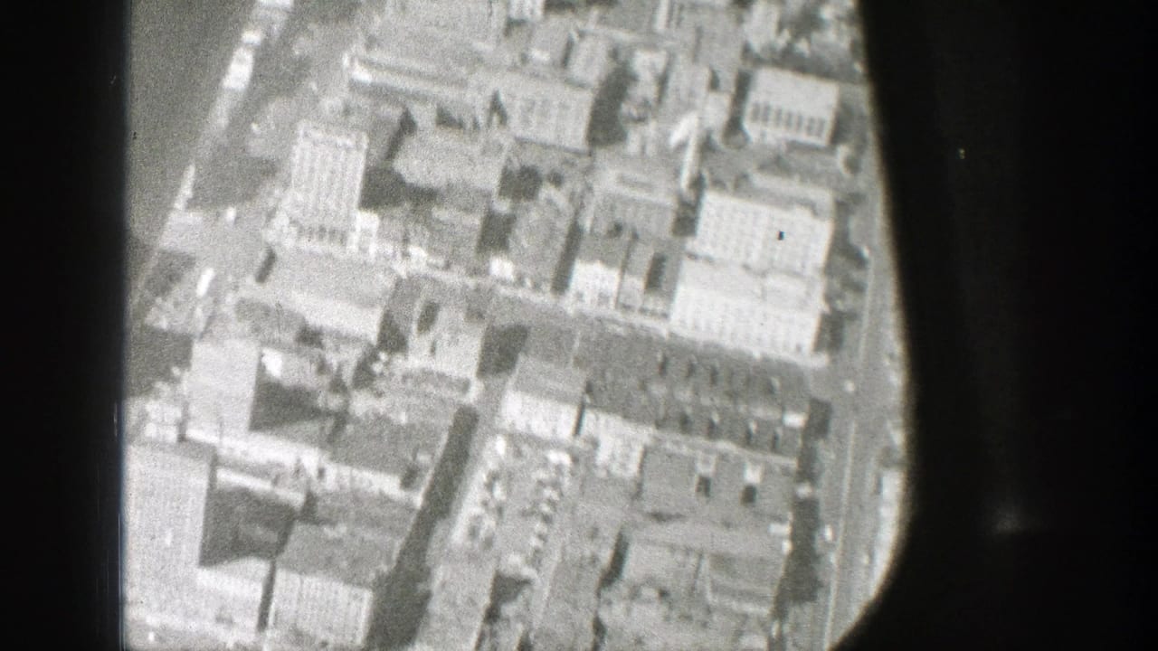 Aerial view of city blocks seen through a dark airplane window frame.
